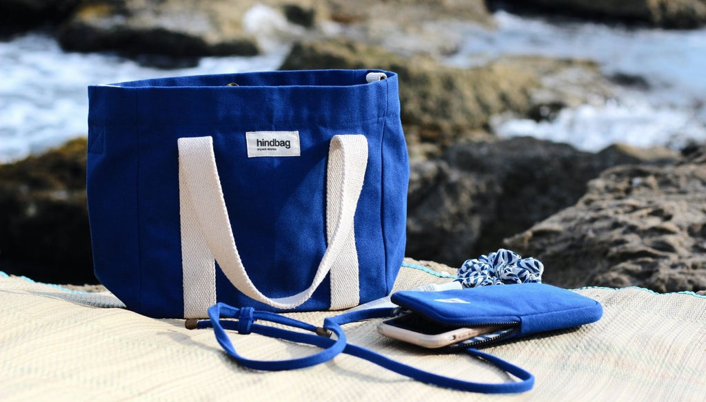 un sac tote bag et une pochette de téléphone de couleur bleu éléctrique, en coton bio, de la marque éco responsable hindbag, posé sur un transat